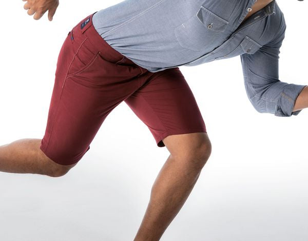 Ein Mann trägt einen grauen Hemd und rote Shorts, er befindet sich in einer dynamischen, sportlichen Pose, als würde er rennen oder springen.