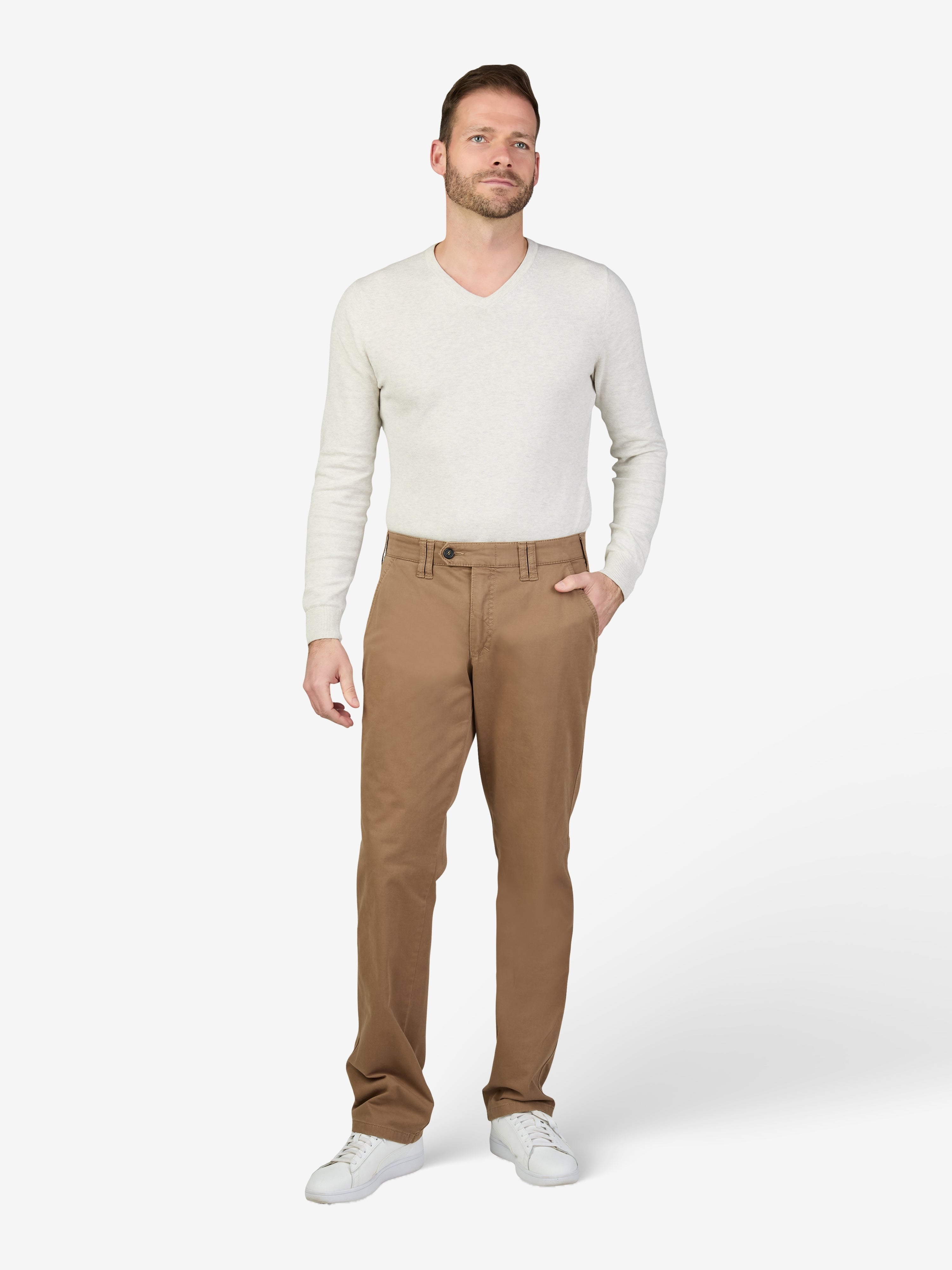 Mann trägt eine beige DENVER 4402 Flat Front-Hose aus Baumwolle mit elastischem Komfortbund, Hemdstopper und Safety-Pocket, kombiniert mit weißem Pullover und Sneakers, vor weißem Hintergrund.