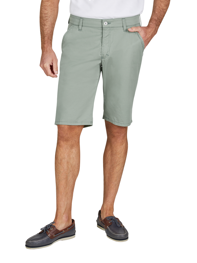 Ein Mann trägt eine hellgrüne, knielange Shorts aus leichtem Stoff, mit Seitentaschen und einem Knopfverschluss. Er hat eine Hand in der Tasche und trägt dunkle Segelschuhe mit Schnürung, Weißmann.