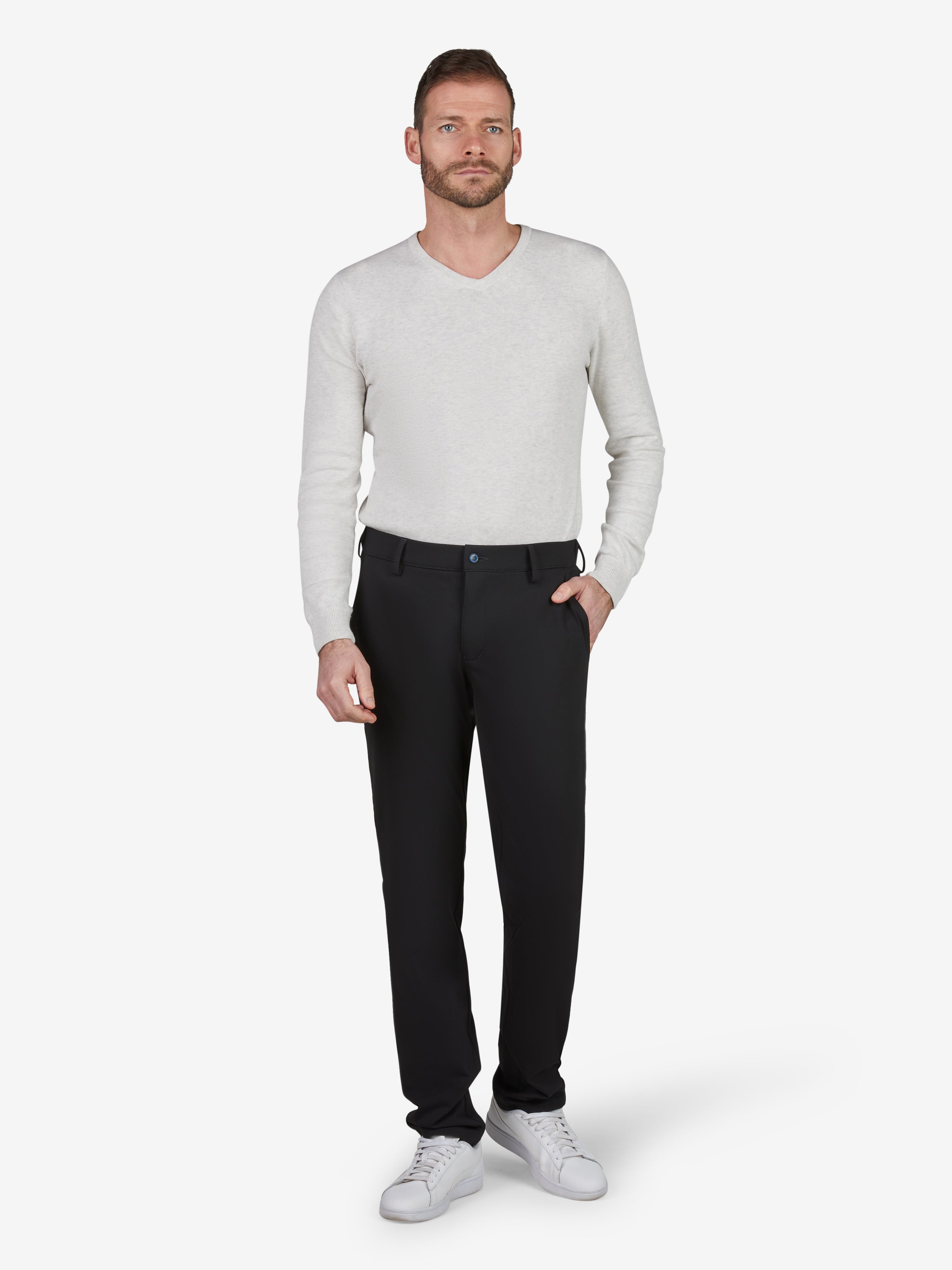 Männlicher Modell trägt schwarze FOXX 8240 Chino-Hose im Slim Fit mit Smokbund, Hemdstopper und mittlerer Leibhöhe, kombiniert mit weißem Pullover und Sneakers, Produktdetails: Superelastisch, Microstruktur, 390 g/lfm, hergestellt von Club of Comfort, ideal für Ganzjahres, schwarz.