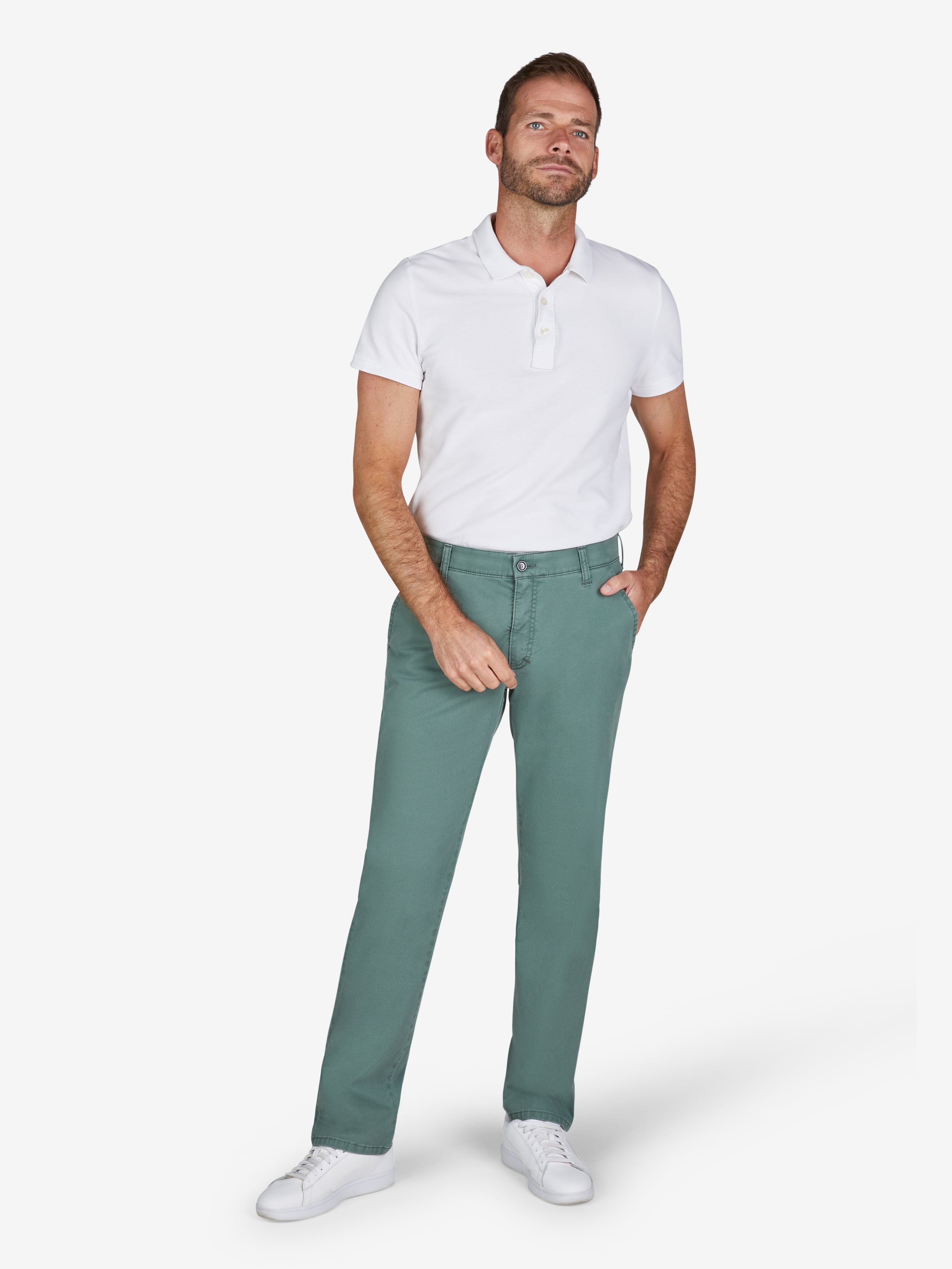 Mann trägt eine grüne GARVEY 7323 Flat Front-Hose aus Baumwolle mit High Stretch, Komfortbund und Hemdstopper, Modell Regular Fit, kombiniert mit weißem Polo-Shirt. Die Hose hat eine schmale Beinpassform, Münztasche rechts, und ist für Frühling/Sommer ideal.