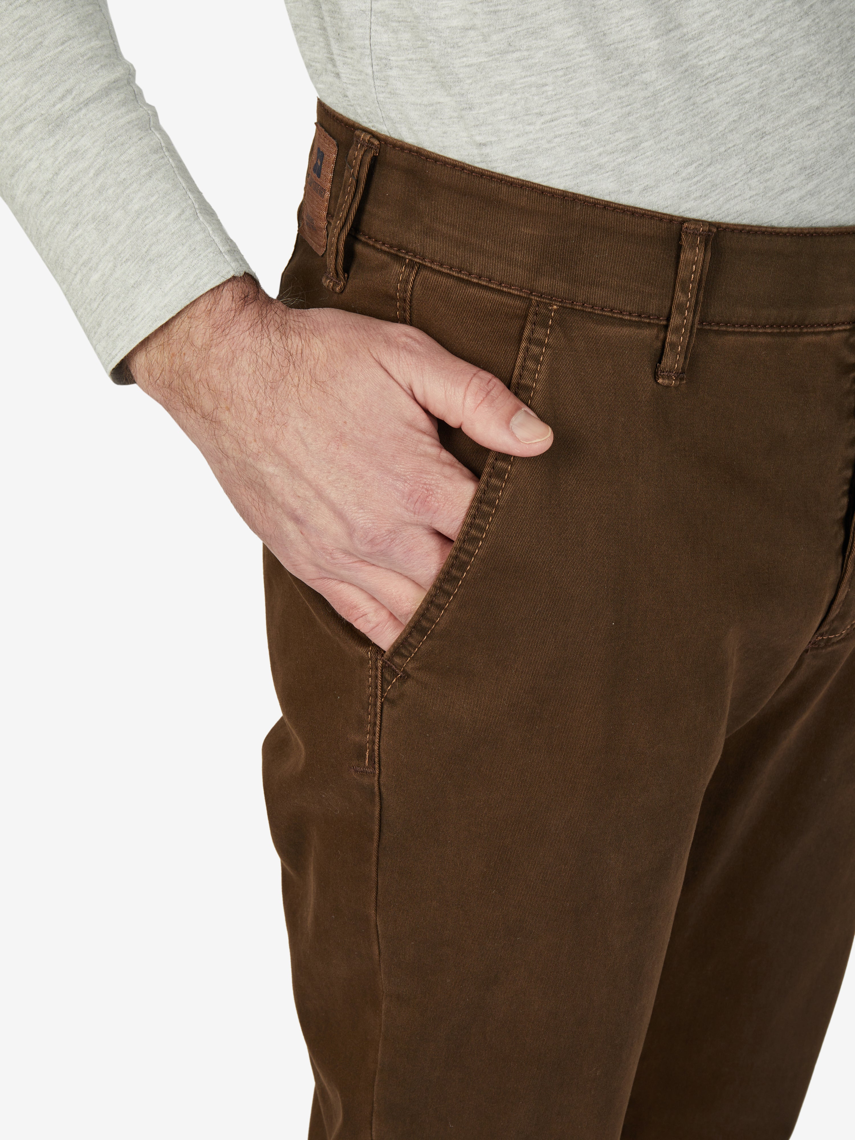Nahaufnahme einer dunkelbraunen Chino-Hose mit elastischem Komfortbund, Hemdenstopper und schmaler Beinführung, getragen von einem Mann in grauem Pullover.