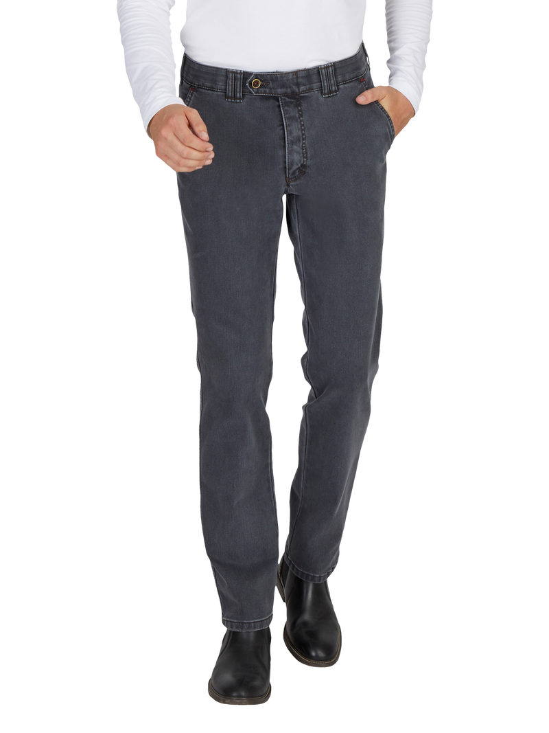 Nahaufnahme eines menschlichen Körpers, der dunkelgraue Jeans trägt, die in der Taille sitzen und leicht locker sitzen. Die Person hat die rechte Hand in der Hosentasche, trägt schwarze Schuhe und ein weißes Langarm-Shirt. Das Bild zeigt nur den unteren Teil des Körpers, ohne Gesicht.