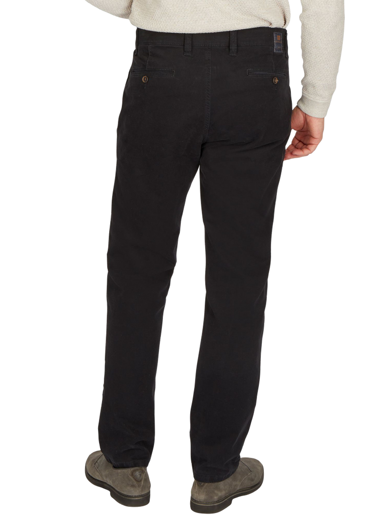 Ein Mann trägt schwarze Jeanshose, die bis zu den Füßen reicht, zusammen mit einer hellgrauen Jacke und grauen Schuhe.