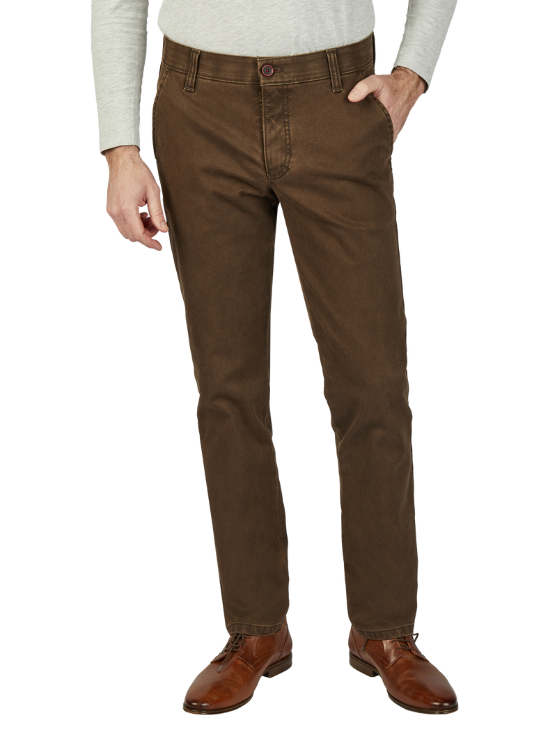 Herren in braunen Jeans, die an der Taille sitzen, mit einer Hand in der Hosentasche. Er trägt braune Lederschuhe und ein hellgraues Oberteil.