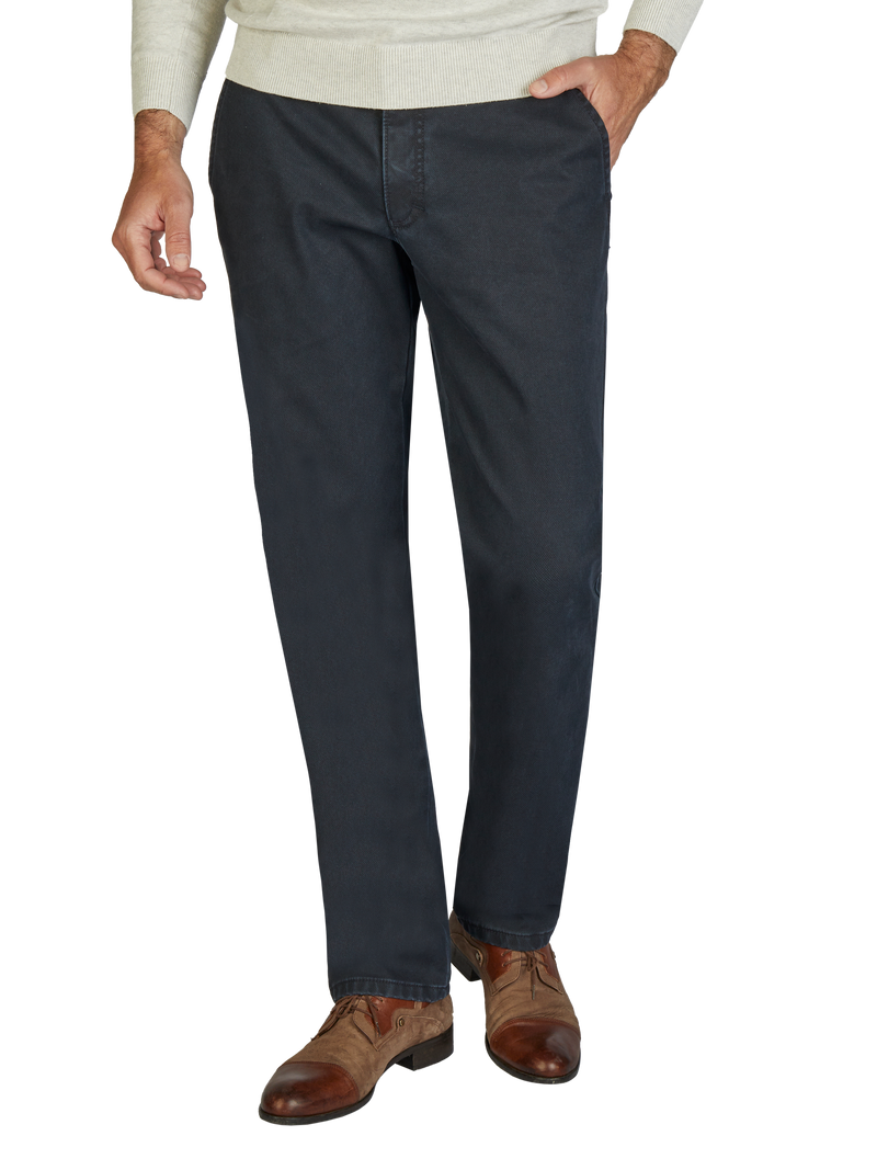 Hose im klassischen Schnitt in Dunkelblau, getragen von einer Person. Die Hose hat seitliche Taschen, sitzt bequem in der Taille und reicht bis zu den Knöcheln. Die Person trägt braune Lederschuhe und einen hellen Pullover.