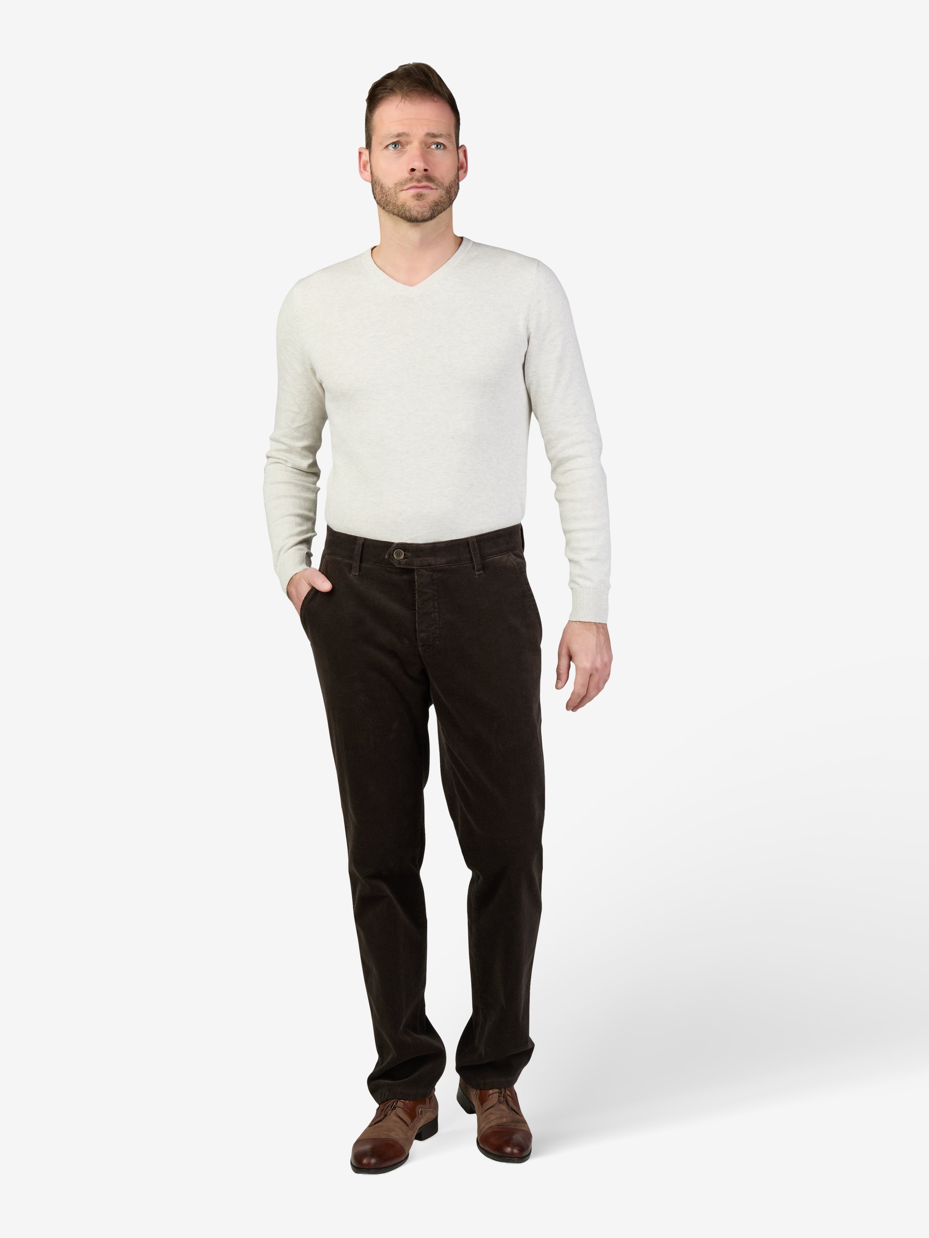 Mann trägt eine graue GARVEY 8200 Flat Front-Hose aus Feincord mit High Stretch, Komfortbund, Hemdenstopper und schmaler Fußweite, kombiniert mit einem weißen Pullover. Die Hose hat eine normale Leibhöhe und ist ideal für Herbst/Winter.