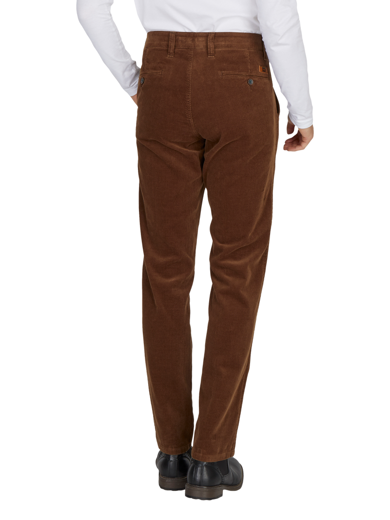 Hinteransicht eines Menschen, der braune Cordhosen trägt, eine weiße Hemdärmel sichtbar sind, und schwarze Schuhe trägt.