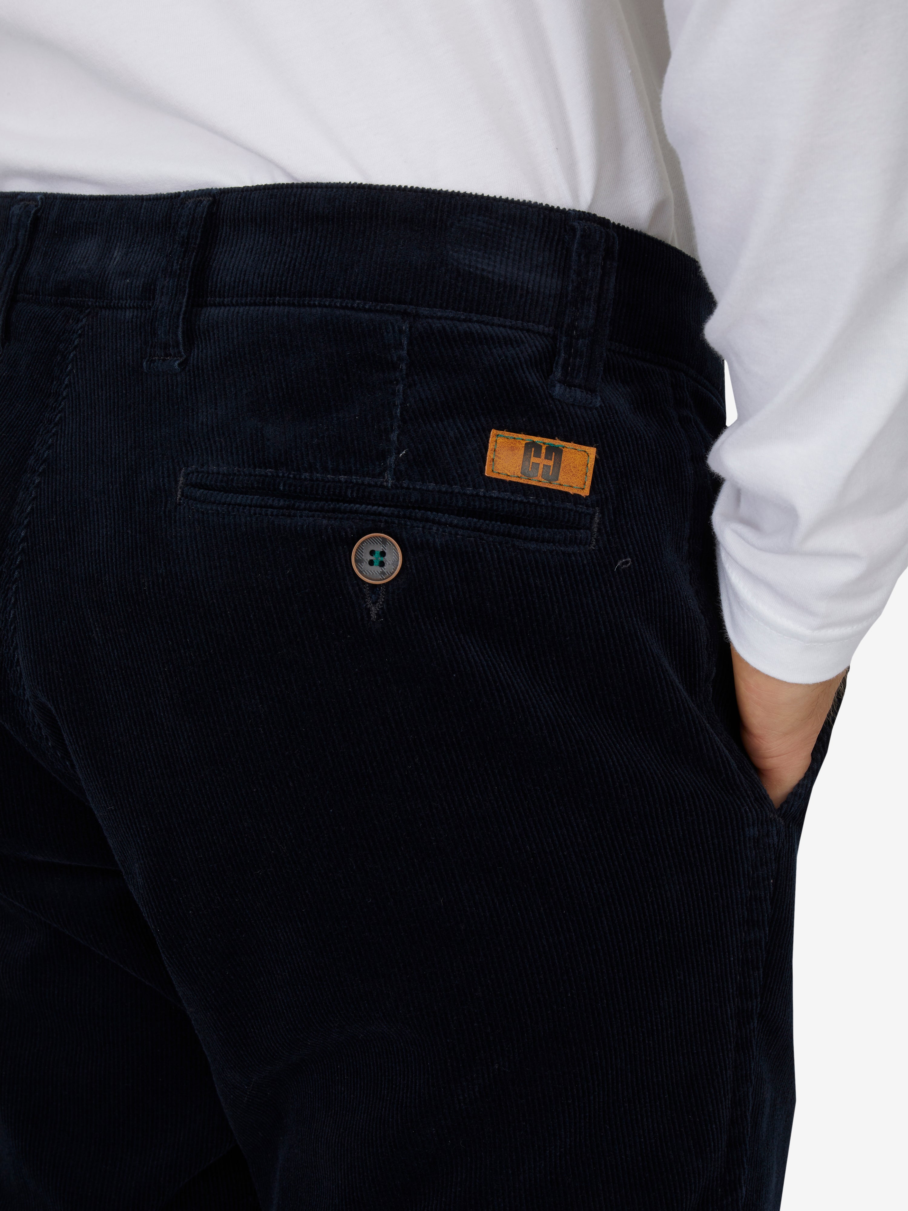 Nahaufnahme einer schwarzen Cord-Hose mit elastischem Komfortbund, Hemdenstopper und Knopf, getragen von einer Person in weißem Hemd, Produktmarkierung "GARVEY 8200" sichtbar.