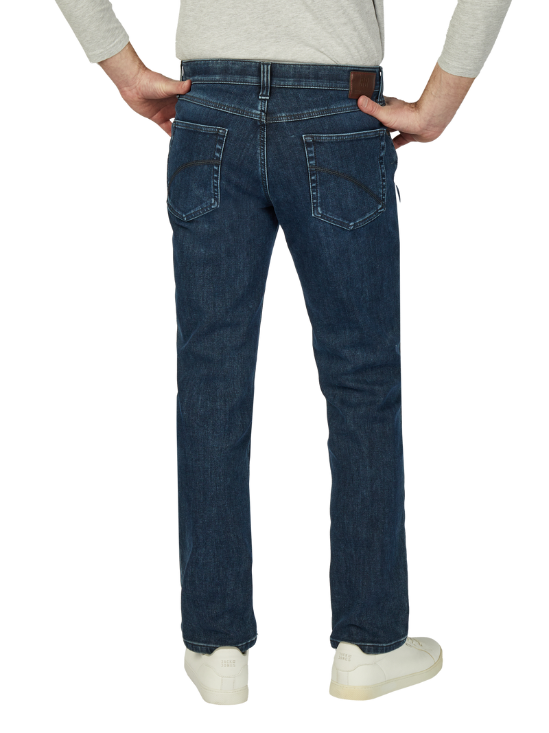 Hüftbereich einer Person in dunklen Blue Jeans mit sichtbaren Rückentaschen, getragen über weißen Sneakers. Die Person hat die Hände in die Taschen gesteckt und trägt ein hellgraues Oberteil.