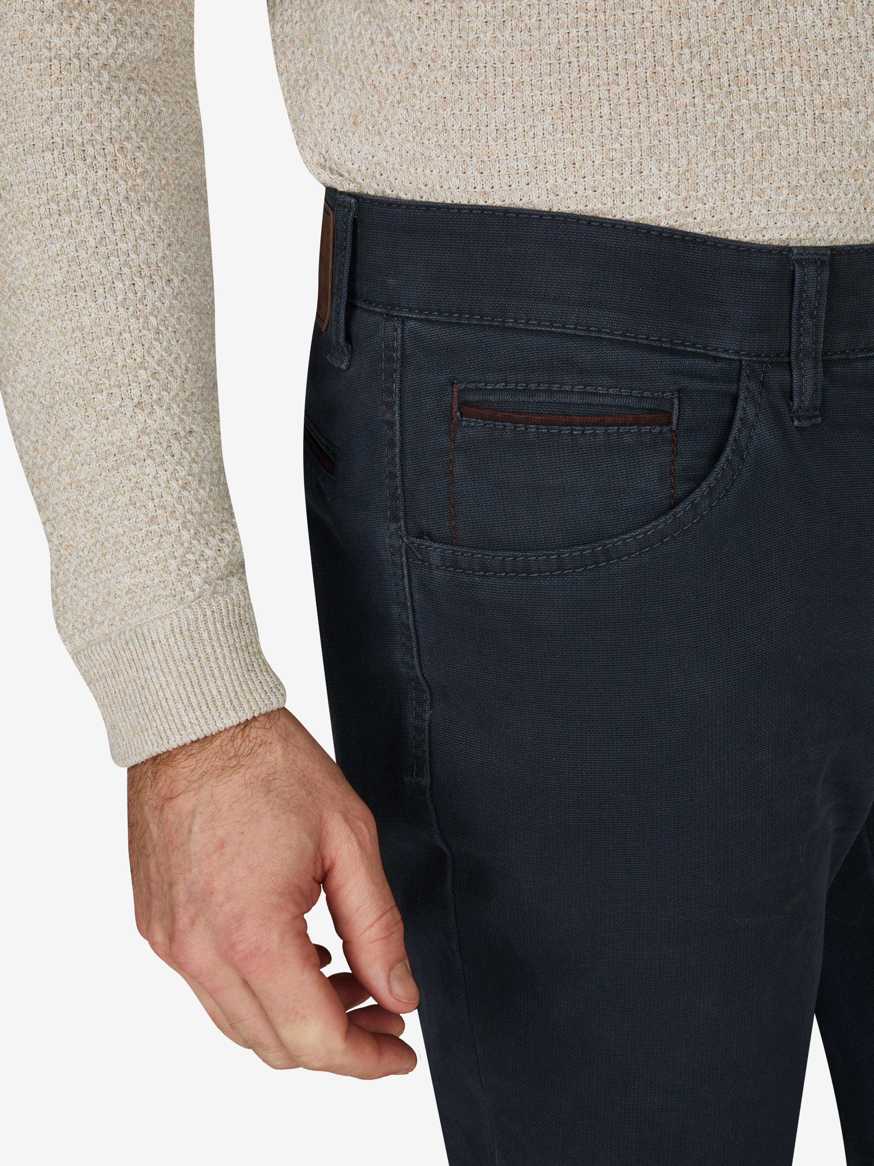 Nahaufnahme einer blauen MARVIN 7218 Hose von Club of Comfort mit modifizierter 5-Pocket-Form, elastischem Comfortbund, Hemdenstopper, doppelter Paspel-Münztasche, High Stretch aus Baumwolle, gewaschen mit Double-Dye-Färbung, normaler Leibhöhe, schlankem Bein, getragen vom Model im beige Pullover, perfekte Herbst/Winter-Hose, made in Green by Öko-Tex.