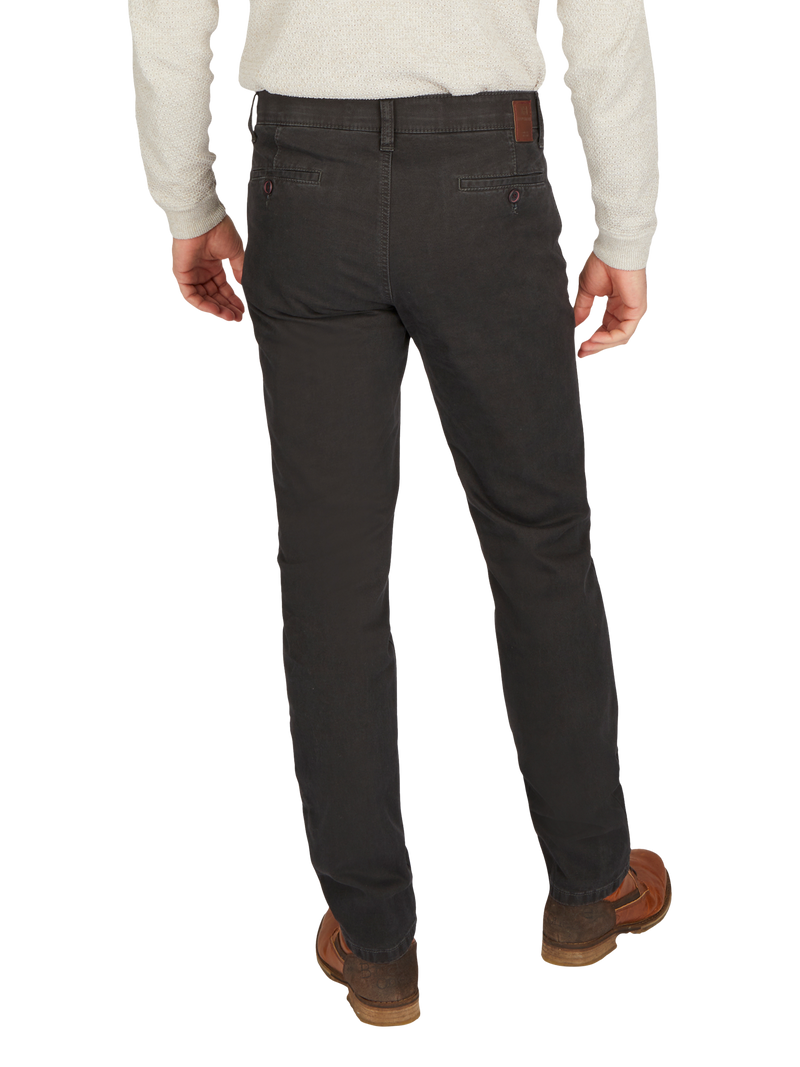 Hinteransicht eines Mannes, der eine beige Strickjacke trägt und eine schwarze Hose, die aus dunklem Stoff besteht. Er steht aufrecht mit den Händen an den Seiten, trägt braune Schuhe und hat eine lockere Haltung.