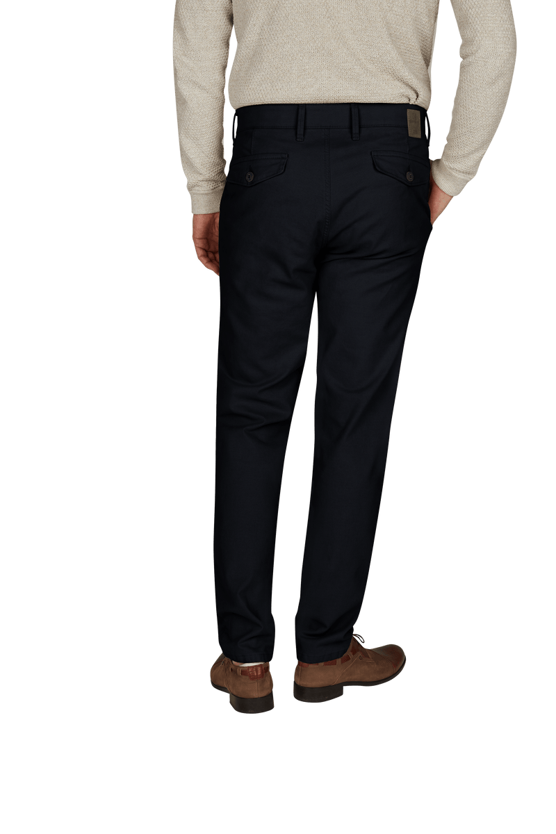 Ein Mann trägt dunkle Anzugshosen, eine beige Pullover und braune Lederschuhe.