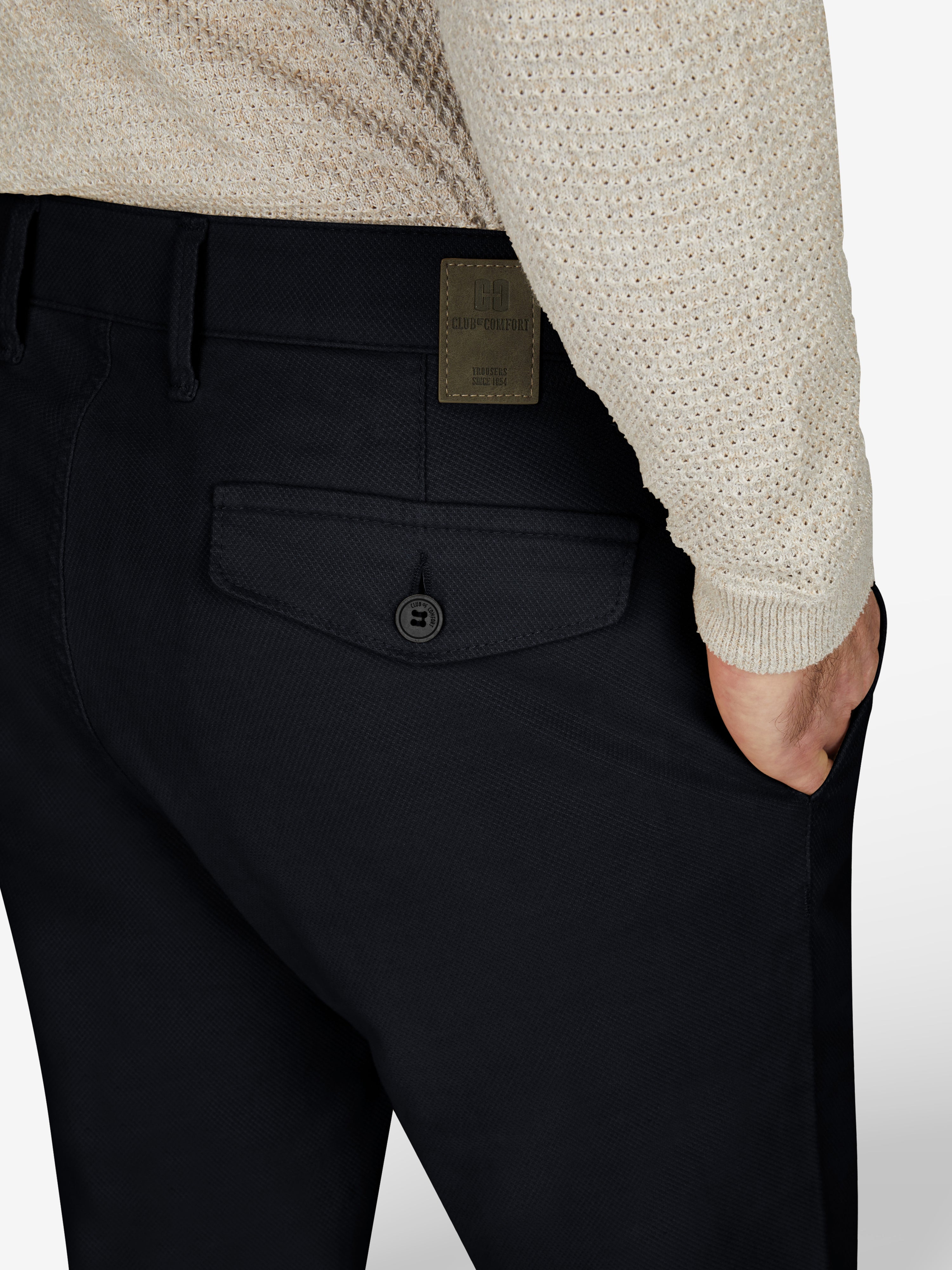 Nahaufnahme einer schwarzen Chinohose von Club of Comfort mit elastischem Comfortbund, Hemdenstopper und Patte mit Knopf auf der Rückseite, modelliert für Herbst/Winter, in Tapered Fit, aus High Stretch Baumwolle.