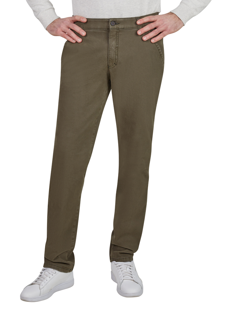 Blick auf eine Person, die bequeme, braune Chino-Hosen trägt, die normal geschnitten sind, mit einer Knopfleiste und seitlichen Taschen. Die Person trägt weiße Sneakers und hat die Hände auf den Hüften.